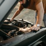 Bearded man doing some spring cleaning under the hood of his car.